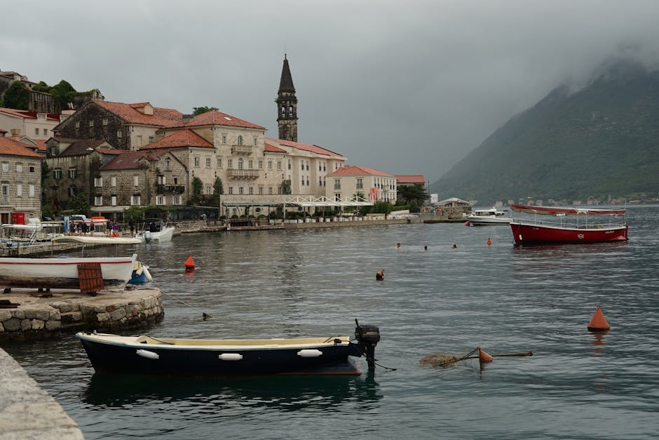 Banchina di Kotor con barche, campanile e montagne nebbiose