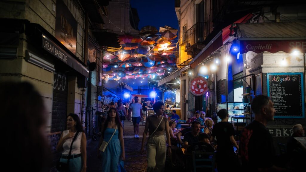 People walking under hanging umbrellas in a lively Tirana night market street