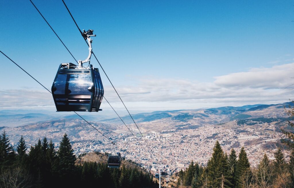 Cable car cabin descending above pine forest with panoramic view of Tirana