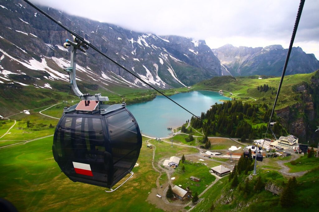 Télécabine noire survolant un lac alpin entouré de montagnes verdoyantes