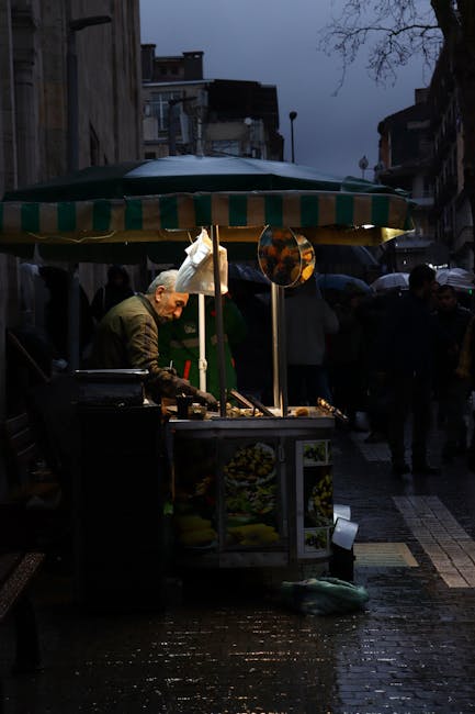 Street vendor grilling food under an umbrella in dim Tirana evening