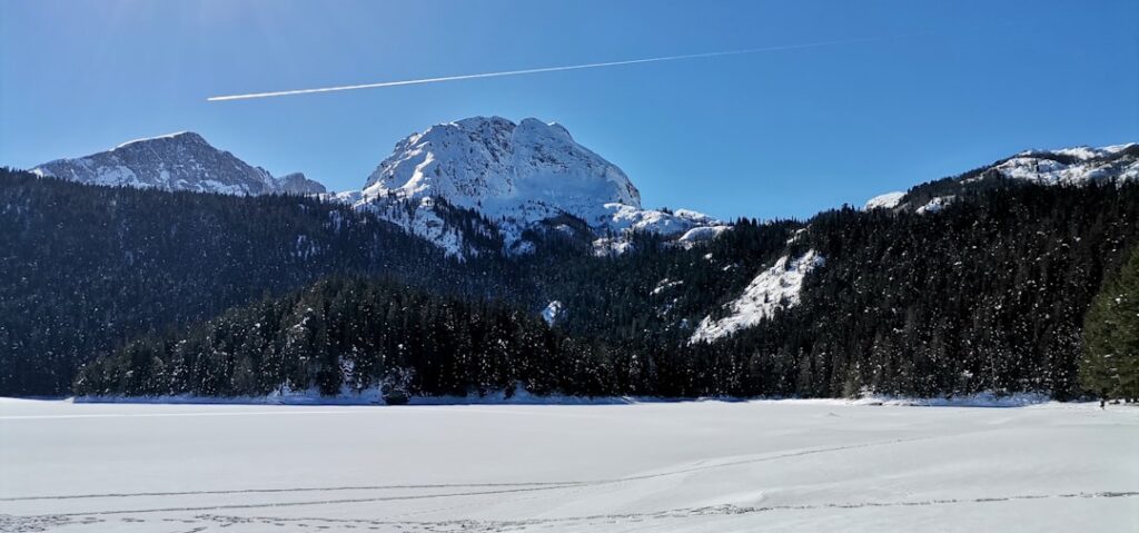 Lago ghiacciato circondato da foreste e cime innevate nel Montenegro