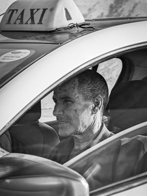 Schwarzweißaufnahme eines nachdenklichen Taxifahrers hinter dem Lenkrad