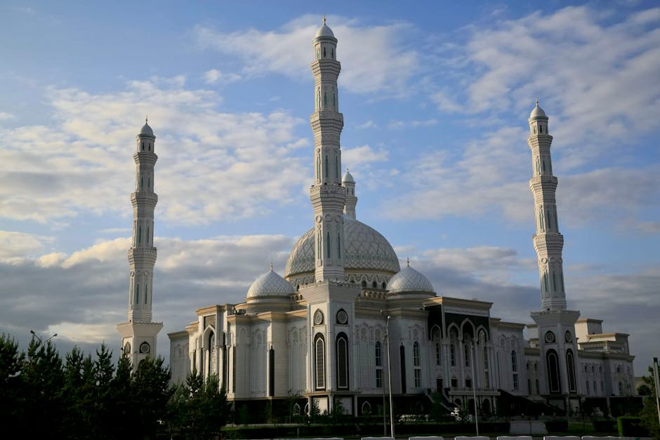 Grand white mosque with central dome and four tall minarets under cloudy sky