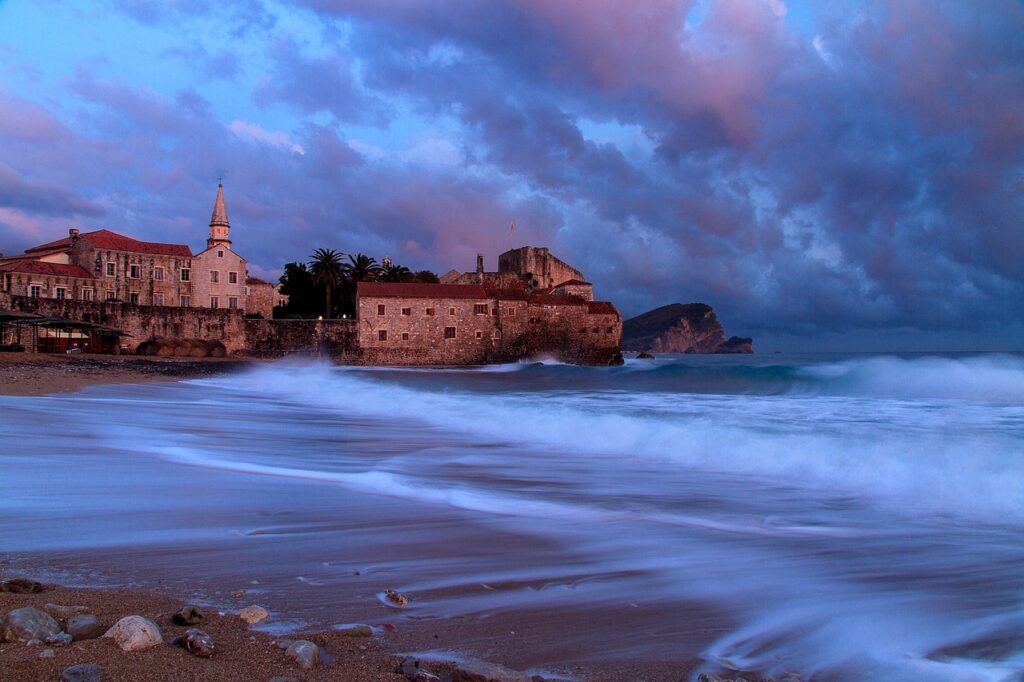 Waves crashing past Budva's seaside old town under purple evening skies, Montenegro