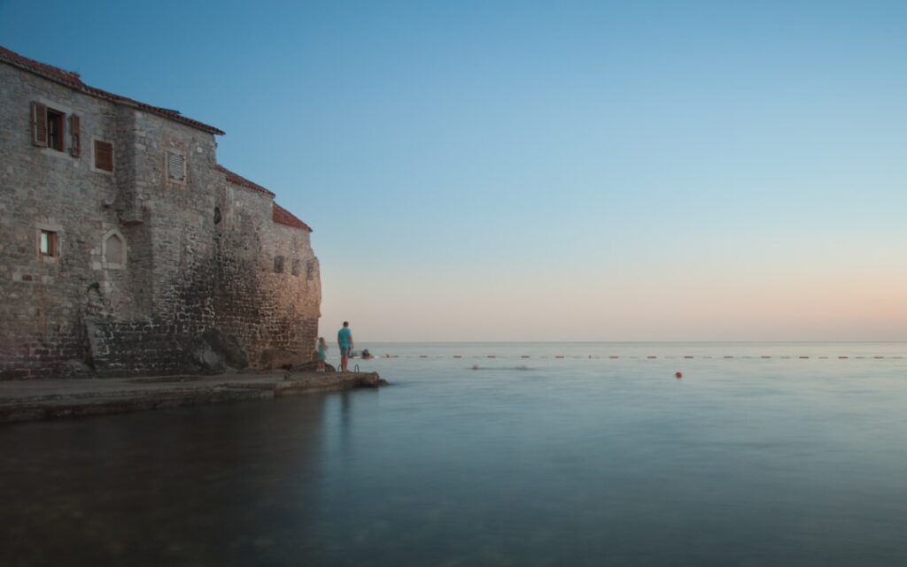 Ancient Budva seaside walls at dusk with people standing on pier