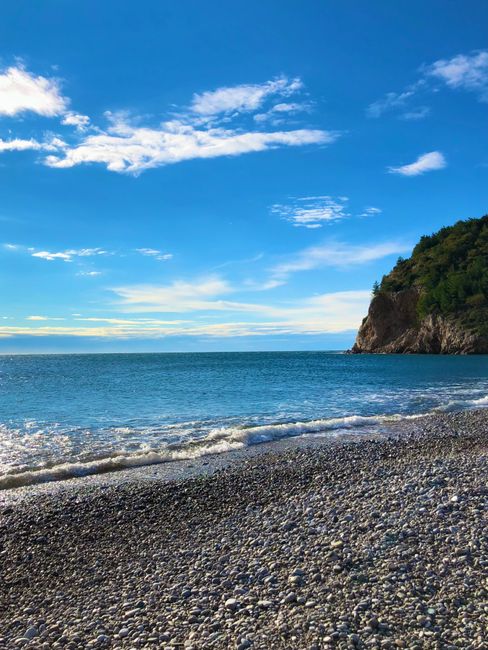 Żwirowa plaża i klif nad turkusowym morzem Czarnogóry.