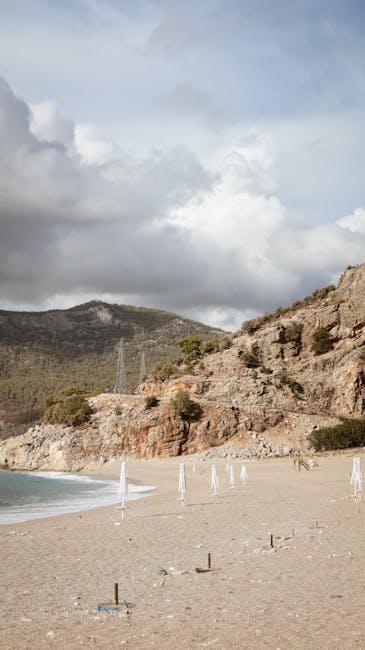 Verlassener Kiesstrand in Montenegro mit zusammengeklappten Sonnenschirmen und Felsen