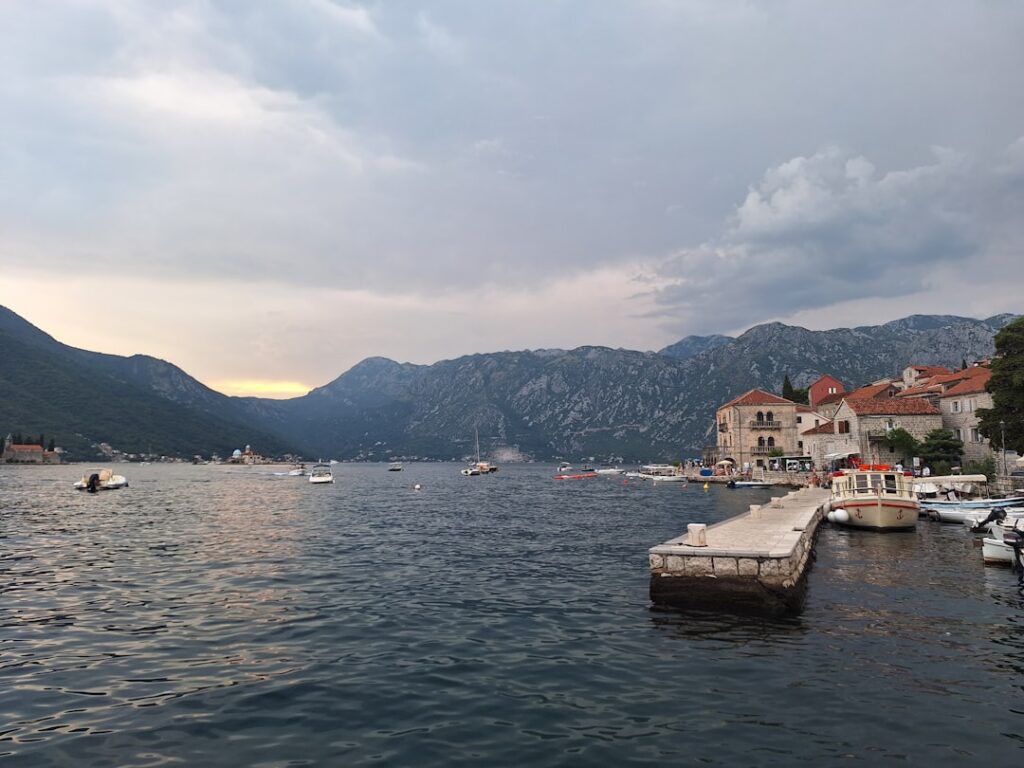 Boats anchored near a stone pier with Montenegrin coastal village