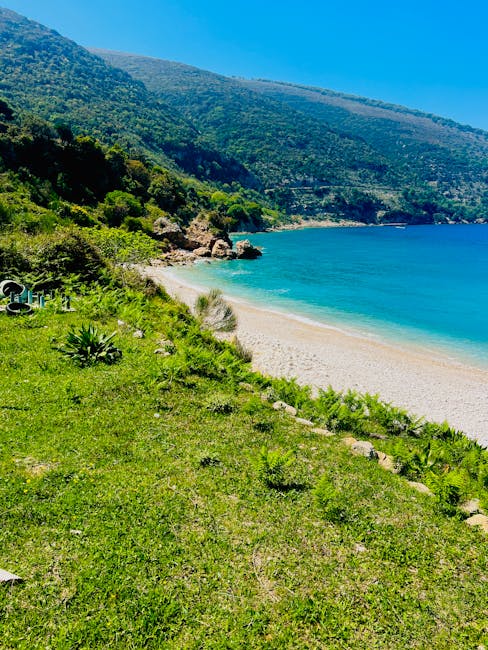 Plage de galets turquoise bordée de prairies et collines en Albanie
