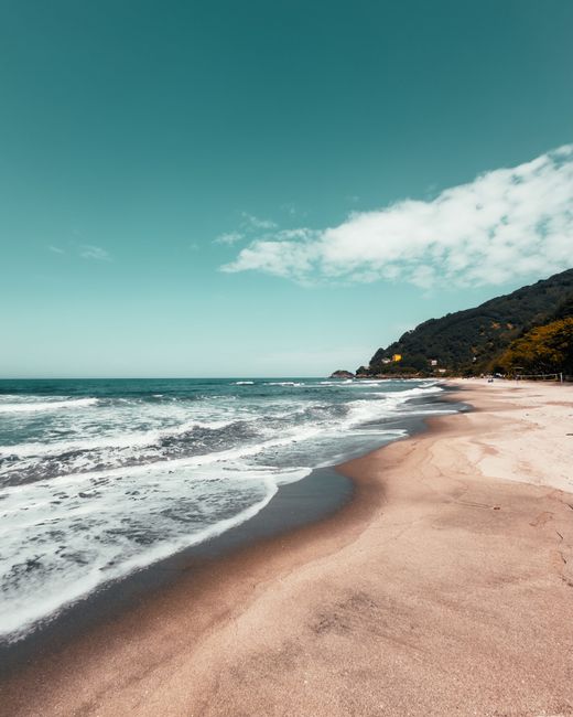 Plage de sable doré avec vagues et collines verdoyantes en Albanie