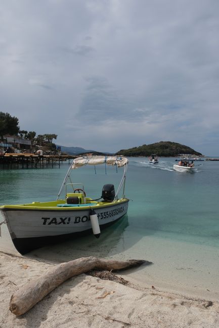 Bateau-taxi amaré sur sable blanc, mer turquoise et îlot en Albanie