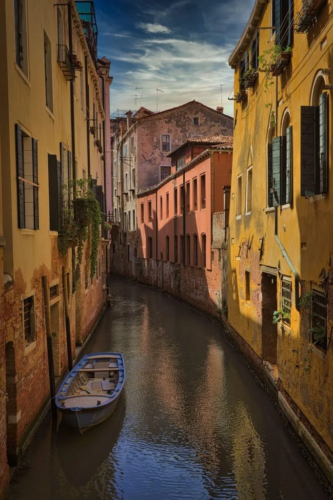 Canal étroit à Venise bordé de façades colorées, barque bleue amarrée.