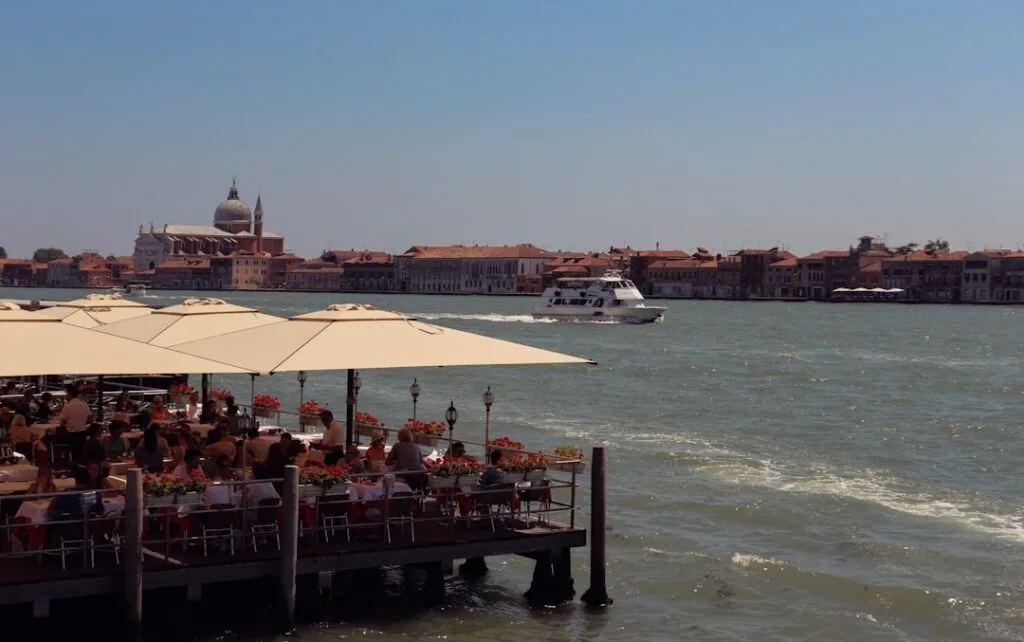 Terrasse de restaurant sur l'eau à Venise, vaporetto et rive opposée.