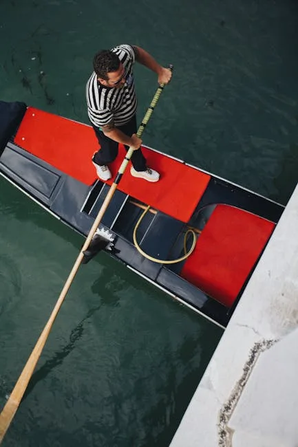Gondolier vêtu de marinière manœuvrant une gondole aux sièges rouges à Venise