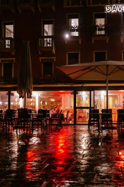Terrasse de café éclairée la nuit, reflets rouges sur sol mouillé à Venise