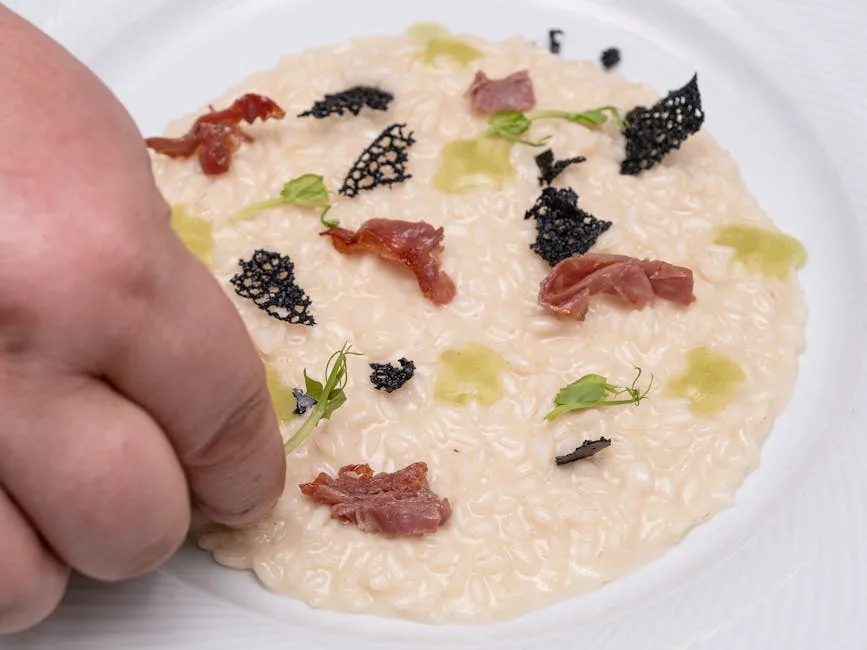 Main du chef ajoutant garnitures sur un risotto crémeux dressé