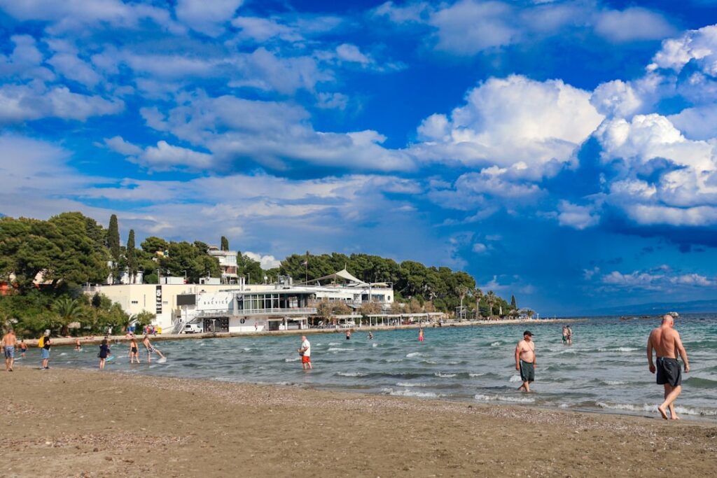 People wading along Bačvice beach in Split under cloudy sky