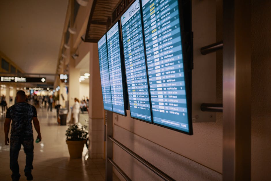 Large airport arrivals display panels with travelers walking past.