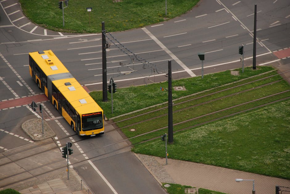 Yellow articulated bus turning at intersection over tram tracks and signals.