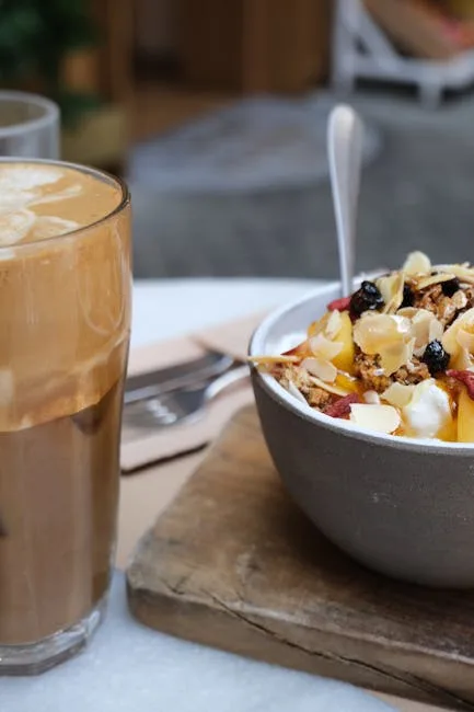 Latte beside a fruit and granola bowl on a wooden board.