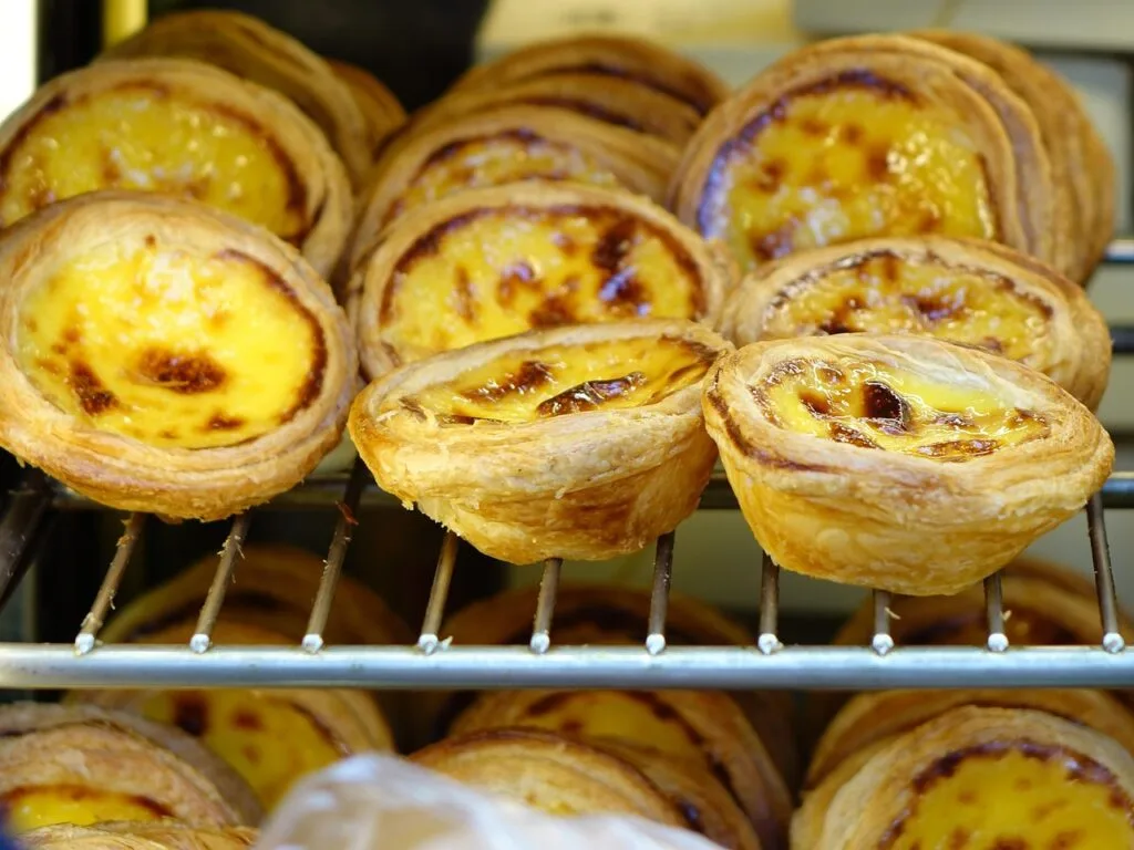 Rows of golden pastéis de nata custard tarts cooling on a rack in Porto