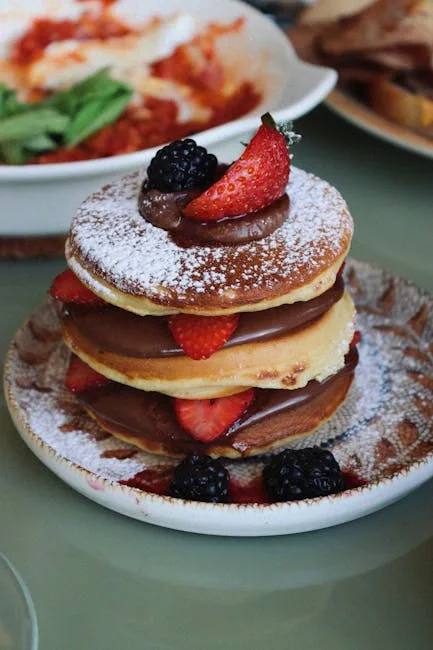 Stack of pancakes layered with chocolate, strawberries, blackberries, powdered sugar