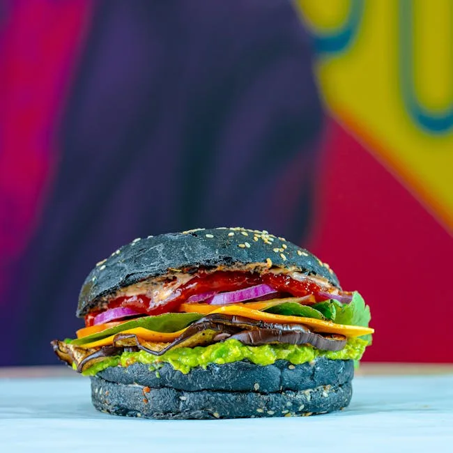 Close-up of a black-bunned vegan burger with avocado and grilled eggplant