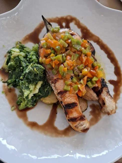 Grilled fish fillets topped with diced peppers and spinach on plate