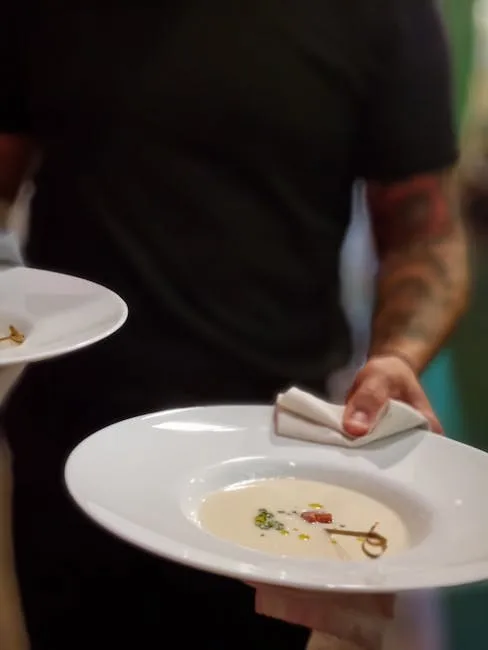 Server holding two white soup bowls, napkin draped over wrist.