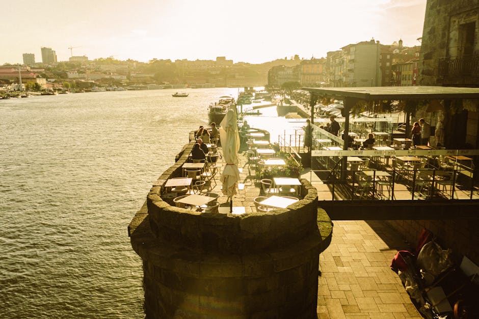 Sunlit riverside terrace overlooking the Douro with empty Porto café tables.