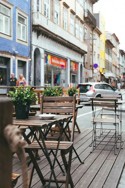 Wooden sidewalk café tables with potted plants on a Porto street.