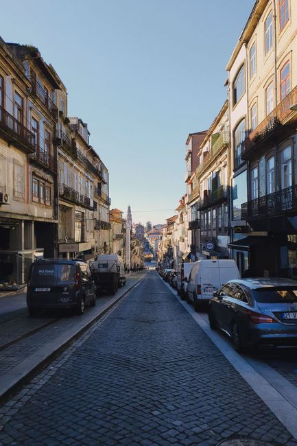 Narrow cobbled street in Porto lined with parked cars and balconies