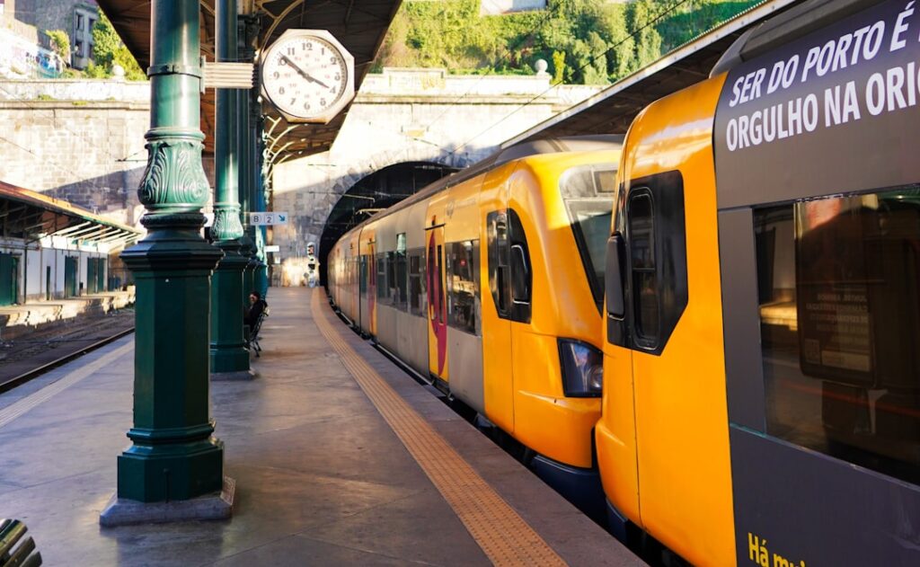 Yellow commuter train at a historic Porto station platform under clock