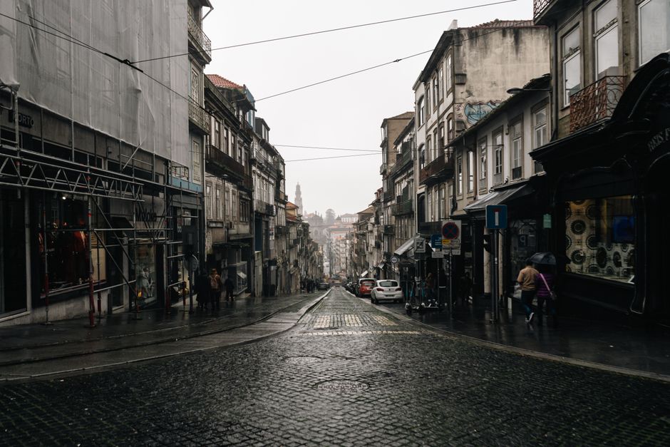 Rain-slick cobbled street sloping down in central Porto under overcast sky