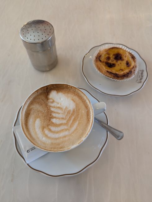 Latte with foam art and pastel de nata on a café table in Porto
