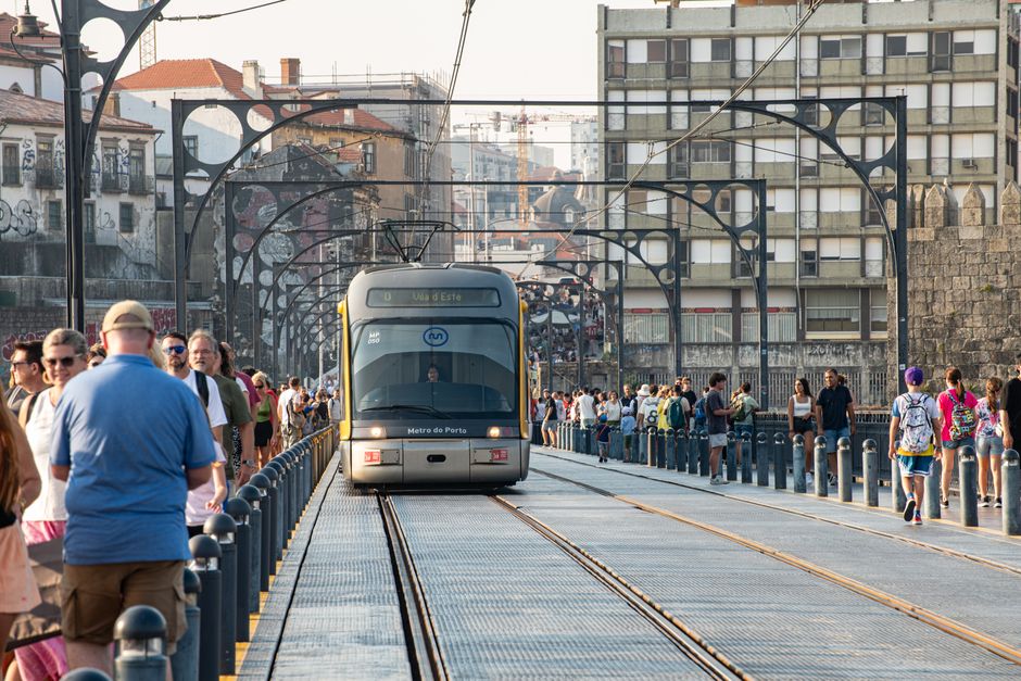 Tram crossing Porto's bridge with crowds of pedestrians on both sides.