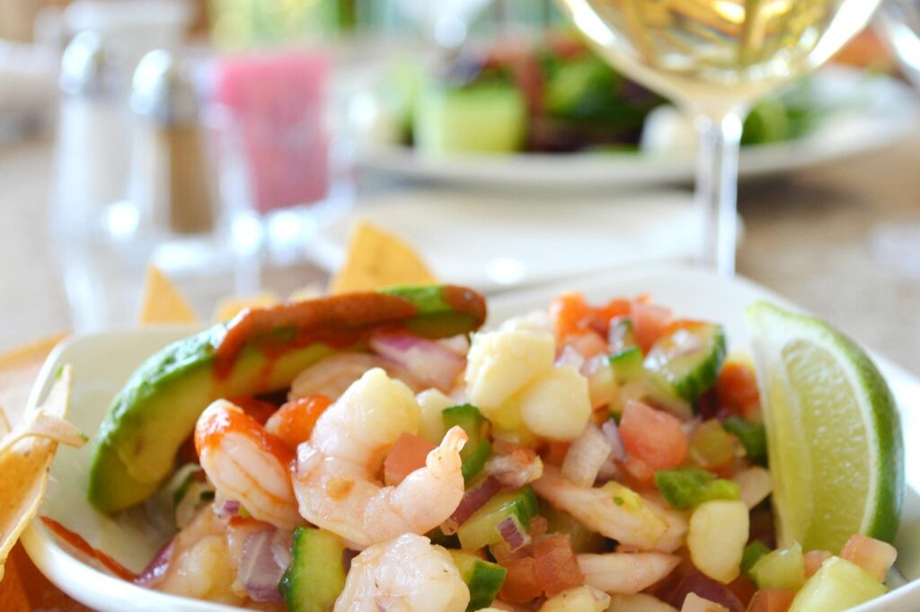 Talerz ceviche z krewetkami i awokado, kieliszek wina w tle