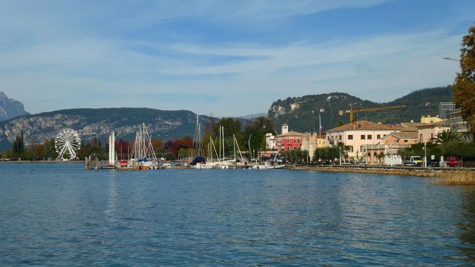 Uferpromenade am Gardasee mit Booten, Riesenrad und Bergen im Hintergrund