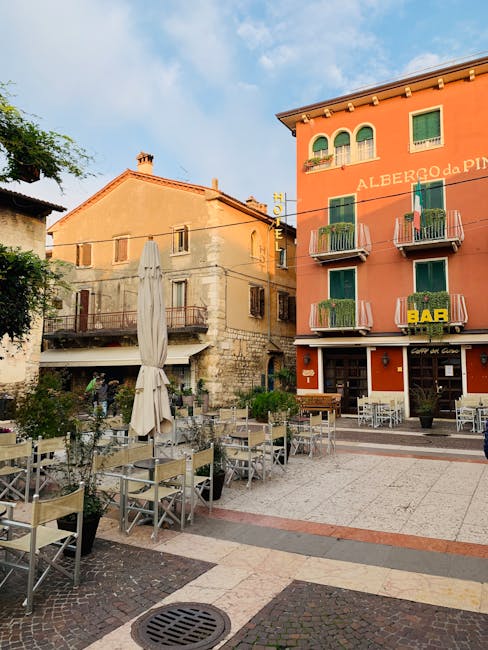 Piazza mit leeren Caféstühlen vor buntem Hotelgebäude im Gardasee-Ortszentrum