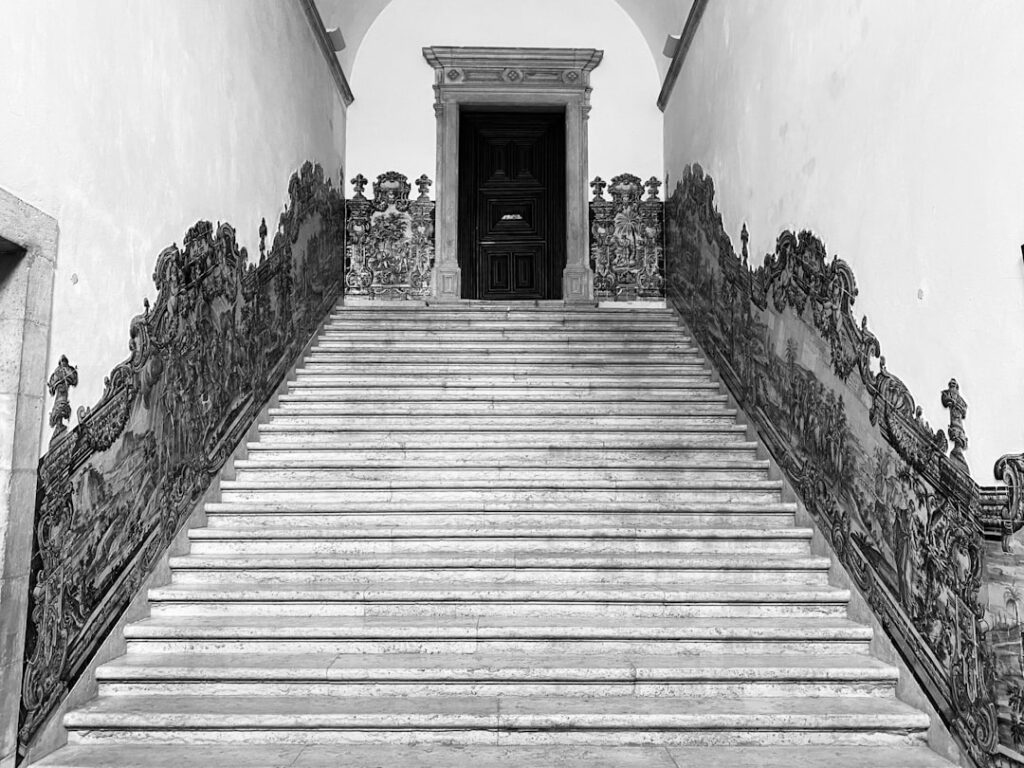 Ornate staircase and historical portraits inside Paço das Escolas